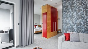A modern hotel room with a bed, a sofa, a dining area, and a large window with curtains.