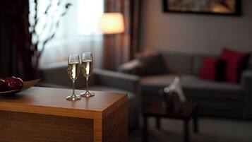 A wooden table with two glasses of a clear liquid, possibly champagne, in a room with a couch and a lamp in the background.