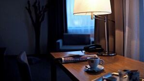A hotel room with a bedside table, a lamp, a cup of coffee, a book, and a telephone.