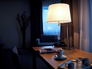Ett hotellrum med ett nattduksbord, en lampa, en kopp kaffe, en bok och en telefon.