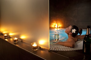 Una persona relajándose en una bañera con velas y una copa de vino.