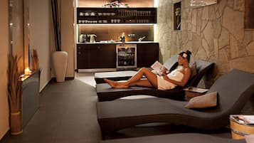 A modern lounge area with a sofa and a reading area, a kitchen in the background, and a decorative vase.