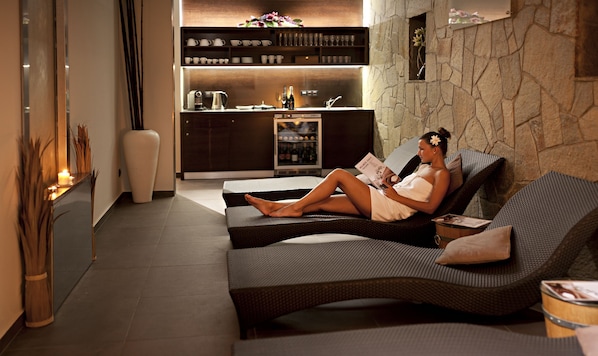 A modern lounge area with a sofa and a reading area, a kitchen in the background, and a decorative vase.