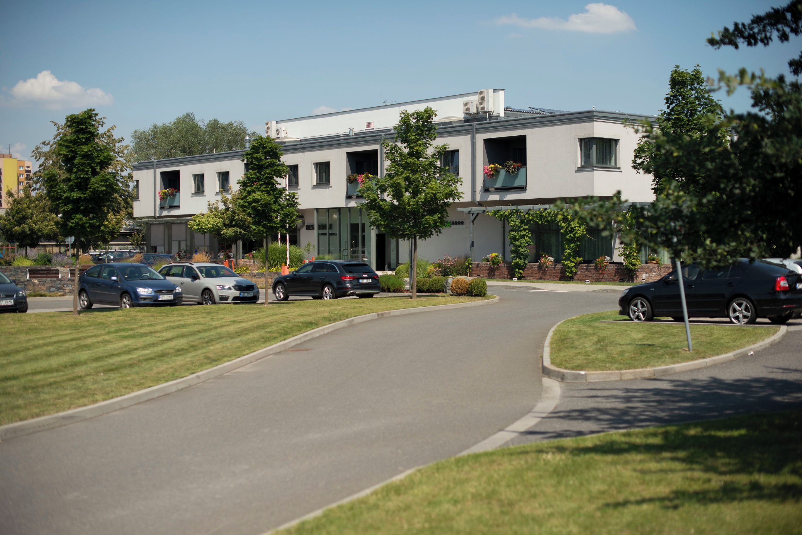 A modern building with a curved driveway, parked cars, and a clear sky.