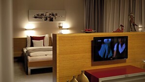 A hotel room with a bed, a TV mounted on a wooden panel, and a small table with decorative vases.