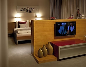 Ett hotellrum med en säng, en tv som är monterad på en träpanel och ett litet bord med dekorativa vaser.