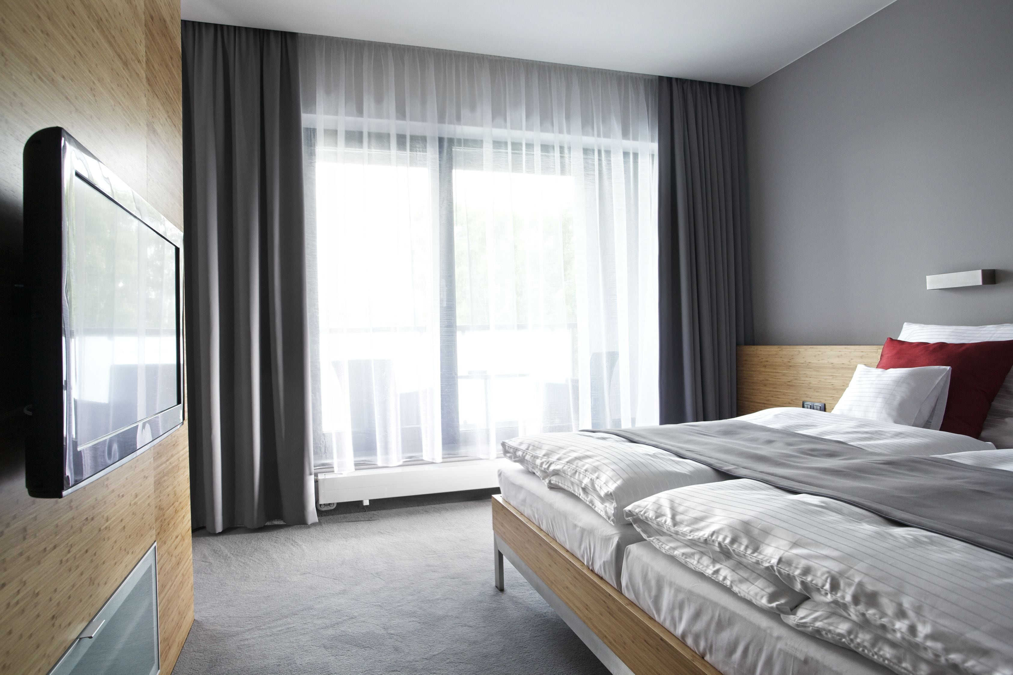 Quarto de hotel com cama, televisão, janela com cortinas e vista para o exterior.