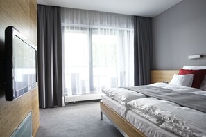 A hotel room with a bed, a TV, a window with curtains, and a view of the outdoors. - Wellness Hotel Abácie Nový Jičín (Novy Jicin)