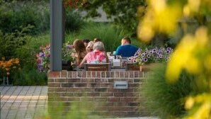 A covered outdoor seating area with a brick wall, surrounded by greenery and flowers. - Wellness Hotel Abácie Nový Jičín (Novy Jicin)