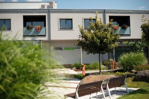 A building with a sign reading 'HOTEL ASACIE,' balconies with flower boxes, and a bench in the foreground.