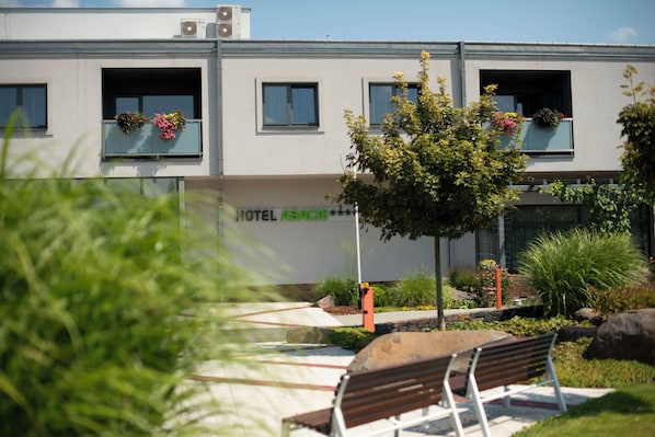 A building with a sign reading 'HOTEL ASACIE,' balconies with flower boxes, and a bench in the foreground.