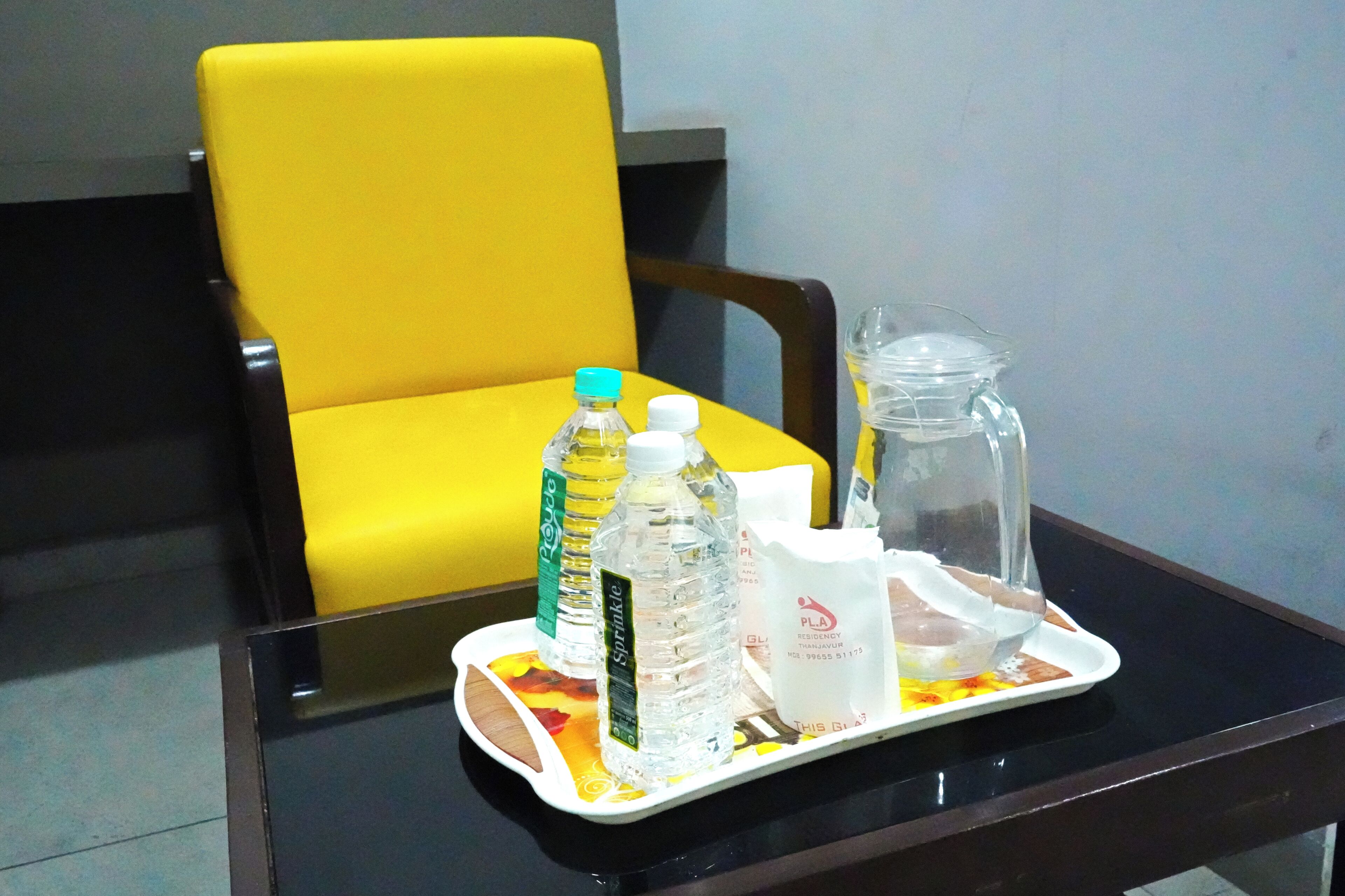 Una bandeja con botellas de agua, una jarra de cristal y una bolsa de papel blanca sobre una mesa.