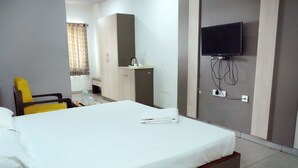A hotel room with a bed, a television mounted on the wall, a desk with a chair, and a wardrobe. - PLA Nest -Comfort Stay (Thanjavur)