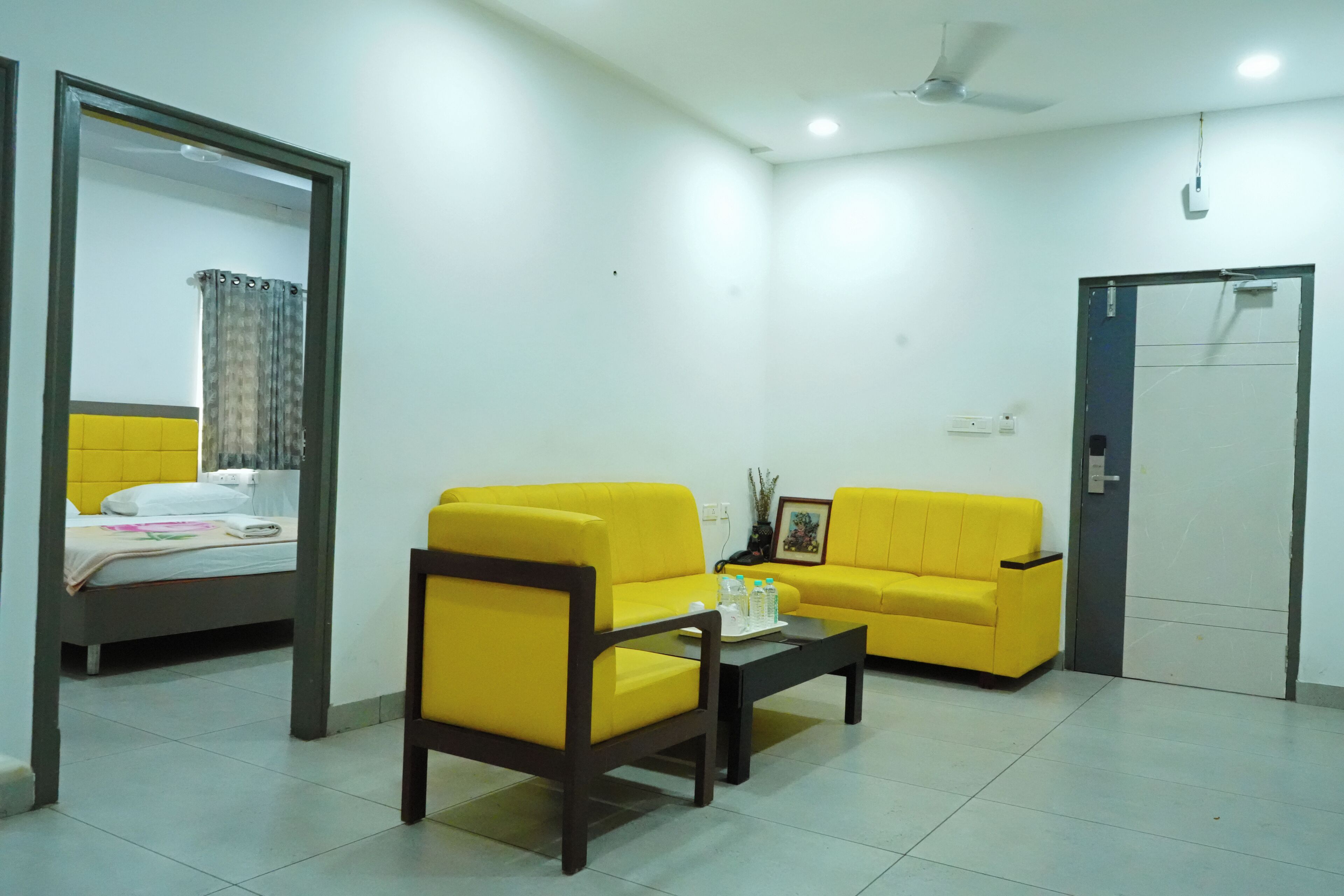 A room with a bed, two yellow sofas, a coffee table, a mirror, and a door.