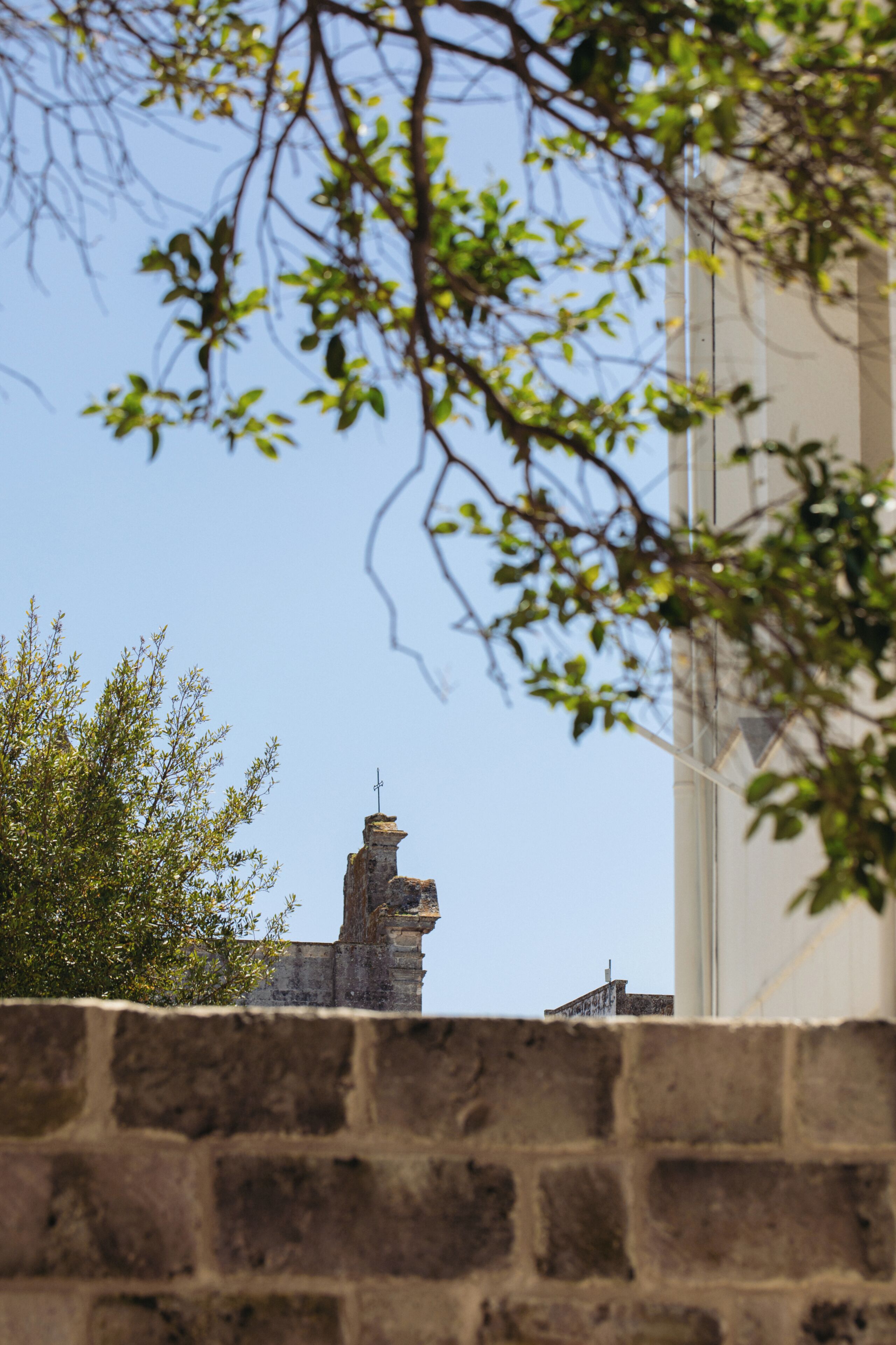 A stone wall with a brick pattern, a clear blue sky, and a building with a chimney in the background.