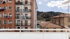 A multi-story residential building with balconies, a river, and a hilly landscape in the background. - Iñaki Deuna - baskeyrentals (Ondarroa)