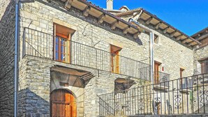 A stone building with a wooden door, a balcony with metal railings, and a window with a wooden shutter. - Cozy Stone House in the Aragonese Pyrenees (Boltaña)