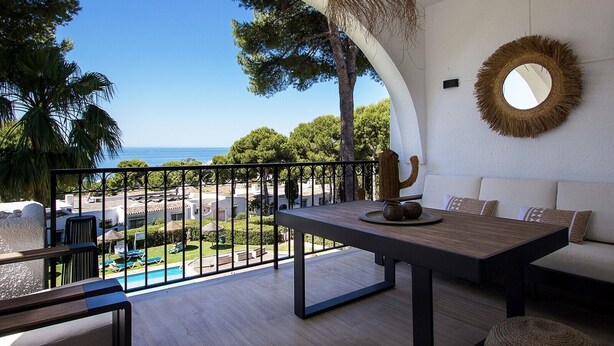 Un balcone con vista sul mare, una decorazione a forma di cactus, uno specchio rotondo e un tavolo in legno.