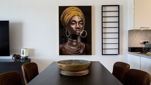 Zona pranzo con tavolo, sedie, un'ampia opera d'arte incorniciata, una ciotola decorativa e un televisore su un mobile.