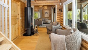 A log cabin interior with a central wood-burning stove, a sofa, and a dining area.