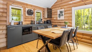 A log cabin interior with a kitchen and dining area, wooden walls, and a view of trees.