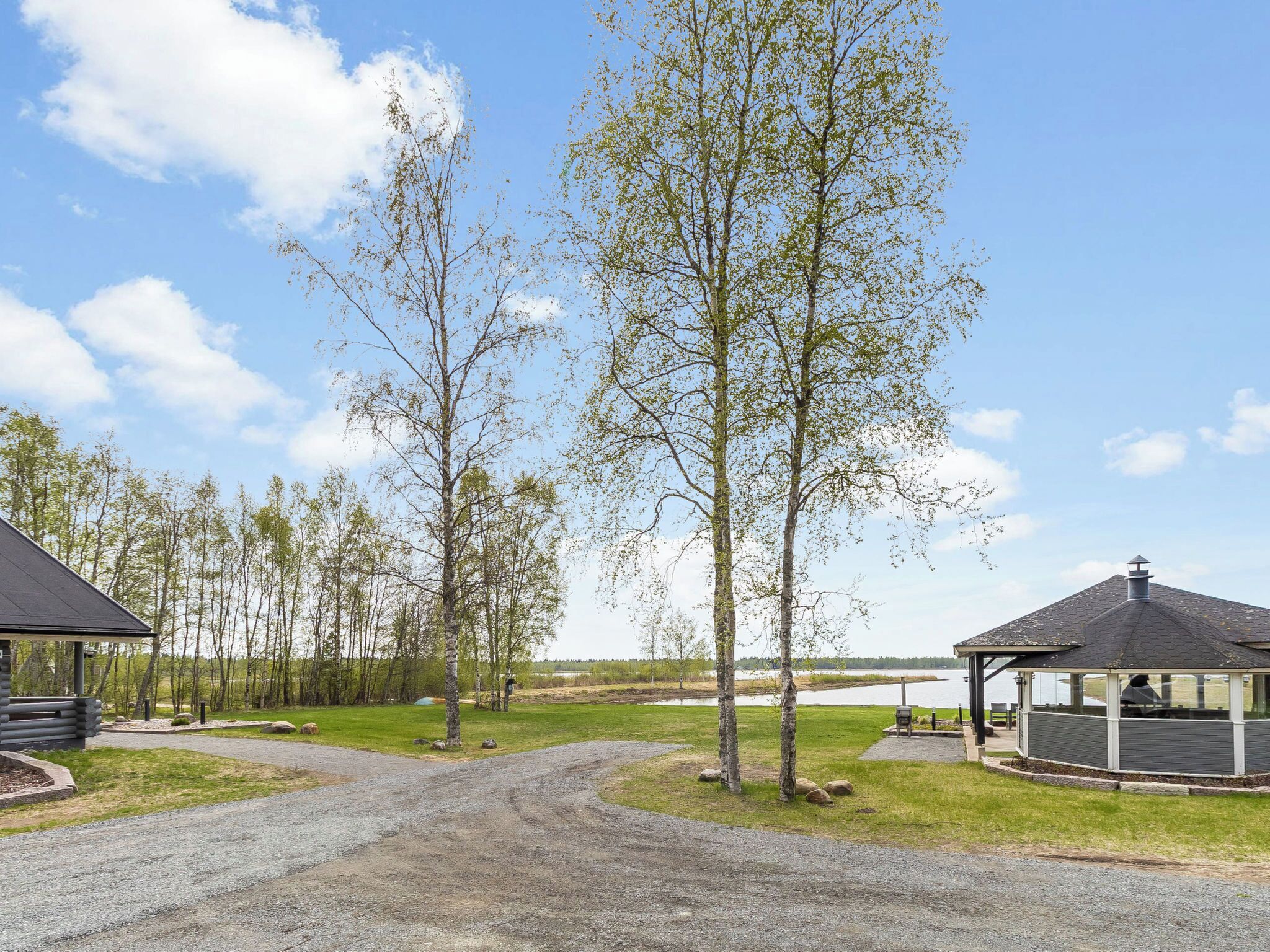 A campground with a gravel path, wooden cabins, and a covered pavilion.