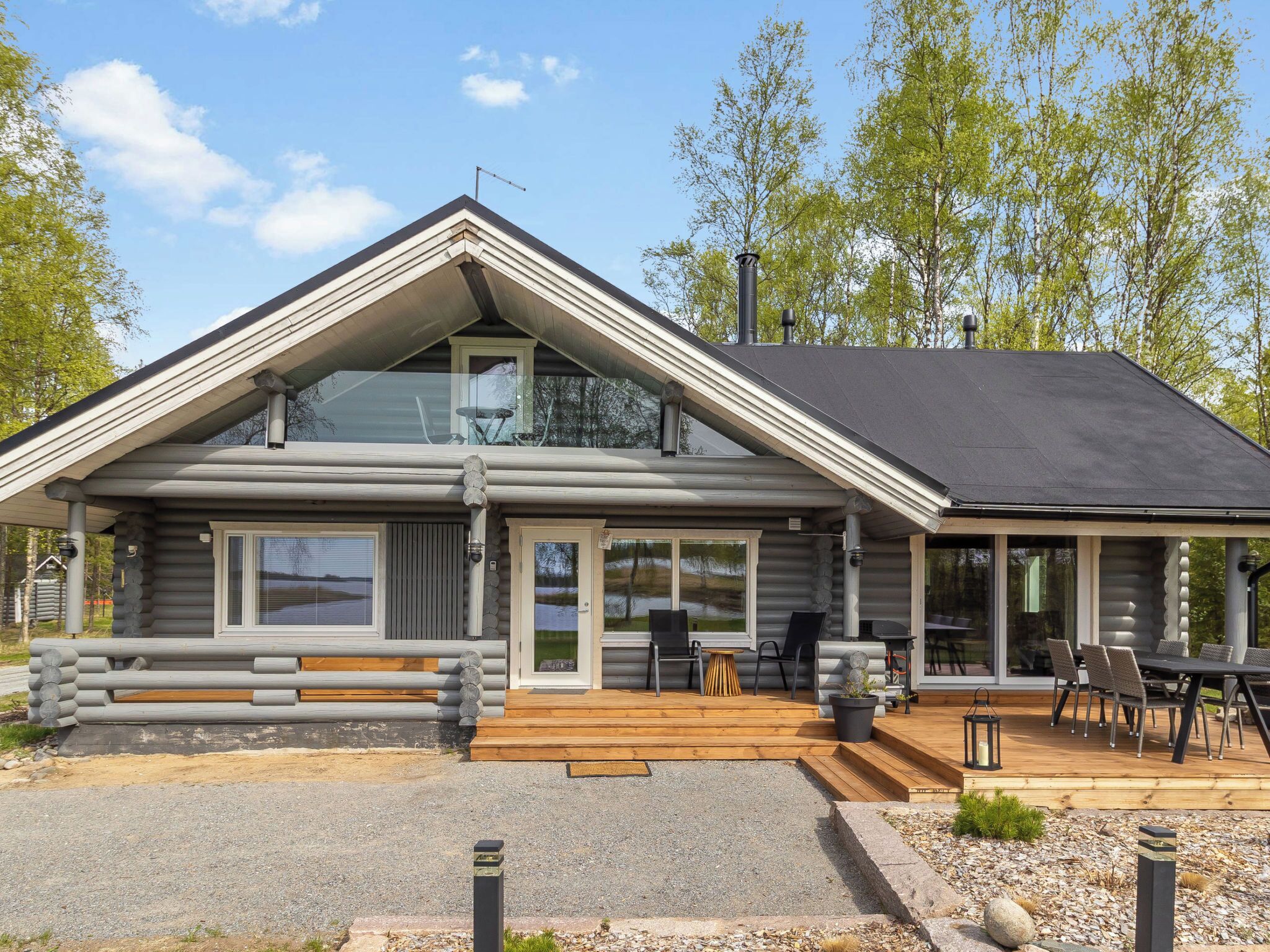 A log cabin with a large deck, a covered outdoor seating area, and a view of the surrounding landscape.
