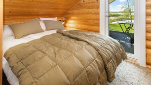 A cozy bedroom with a bed, pillows, a bedside lamp, and a view of a grassy area through a glass door.