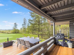 Un espace extérieur abrité, équipé d’une table et de chaises, d’un barbecue et offrant une vue sur un terrain de golf.