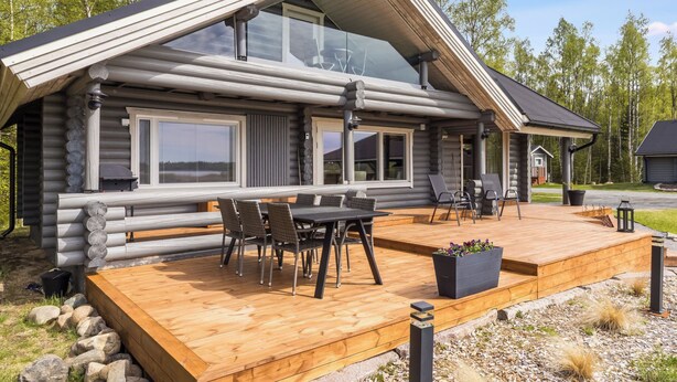 A log cabin with a deck, outdoor seating, and a large window.