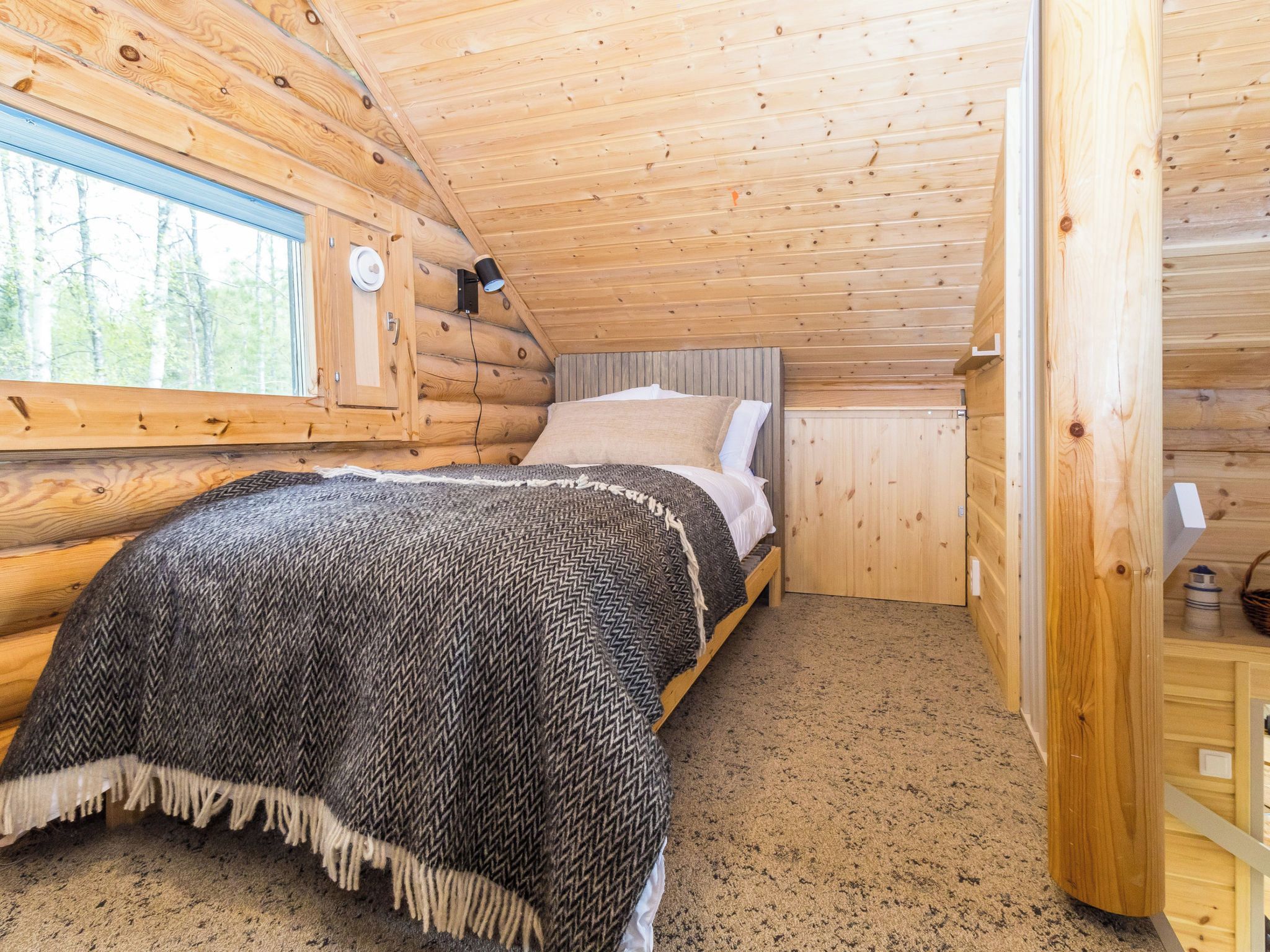 Een slaapkamer in een blokhut met een bed, een raam en een houten plafond.