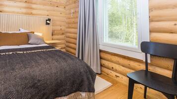 A log cabin room with a bed, a desk, a chair, and a window with curtains.