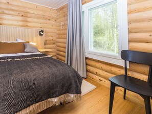 Una habitación tipo cabaña de madera con cama, escritorio, silla y ventana con cortinas.