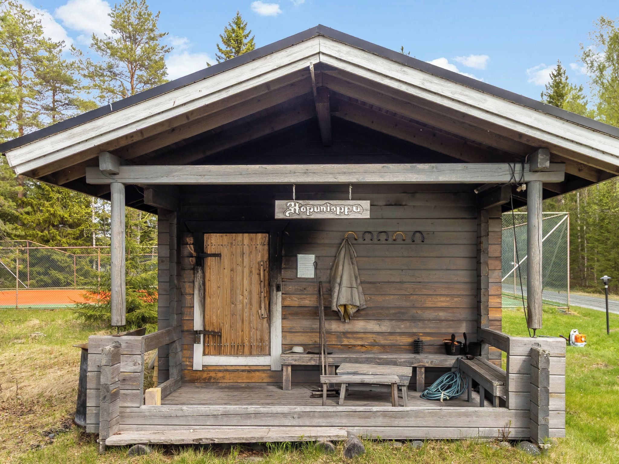 Uma cabana de madeira com varanda, uma placa com a inscrição 'Hopunloppu' e um banco.