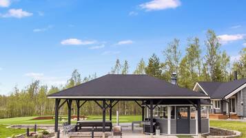 A covered outdoor seating area with a grill, benches, and a view of a golf course.