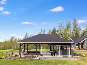 Ett takförsett utomhusområde med sittplatser, en grill, bänkar och utsikt över en golfbana.