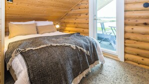 A log cabin bedroom with a bed, a nightstand, a lamp, and a sliding glass door to an outdoor patio.