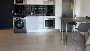 A modern kitchen with a washing machine, oven, and microwave. There is a dining area with a table and chairs.