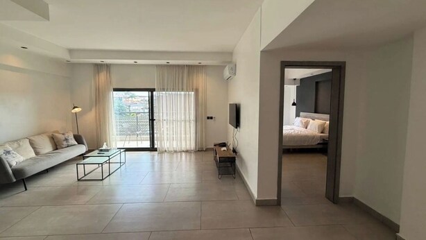 A modern living room with a sofa, coffee table, and a TV. There's a sliding glass door leading to a balcony.