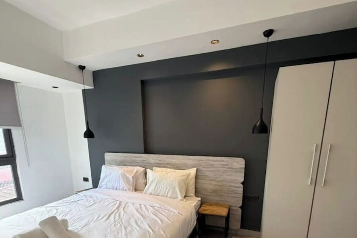 A modern bedroom with a bed, bedside table, wardrobe, and pendant lights.