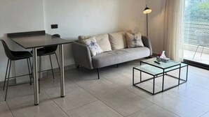 A modern living room with a sofa, a glass coffee table, a dining table with chairs, and a pendant light.