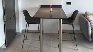 A modern dining area with a dark table, two chairs, a vase with flowers, a hanging light, and a grey sofa.