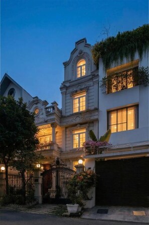 Um edifício clássico com arquitetura elaborada, portão de entrada e um jardim bem cuidado.