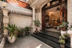 Entrada de hotel com uma escadaria imponente, plantas em vasos e interior bem iluminado.
