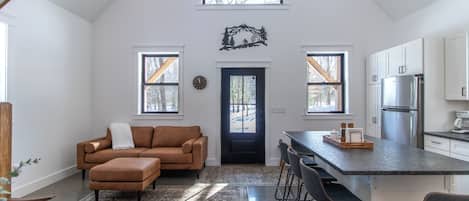 Una cocina amplia con techo alto, una isla central y una zona de estar acogedora con sofá y reposapiés.