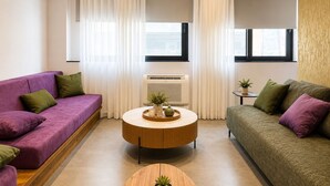 A modern living room with two sofas, a round coffee table, and an air conditioning unit. - Gold & Concrete Acropolis Residence (Athina)
