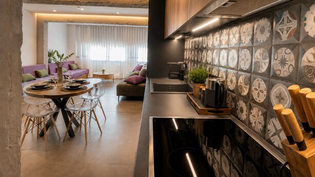 A modern kitchen with a central island, a dining area with a round table and chairs, and a living room with a sofa and a large window. - Gold & Concrete Acropolis Residence (Athina)