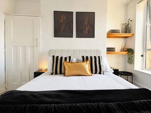 A bed with a black and white striped headboard, a gold accent pillow, and a black throw blanket. There are two framed artworks on the wall above the bed.