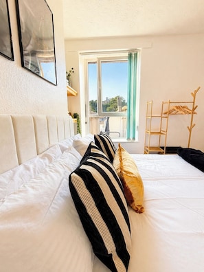 A hotel room with a bed, a window with a view, and a wooden coat rack.