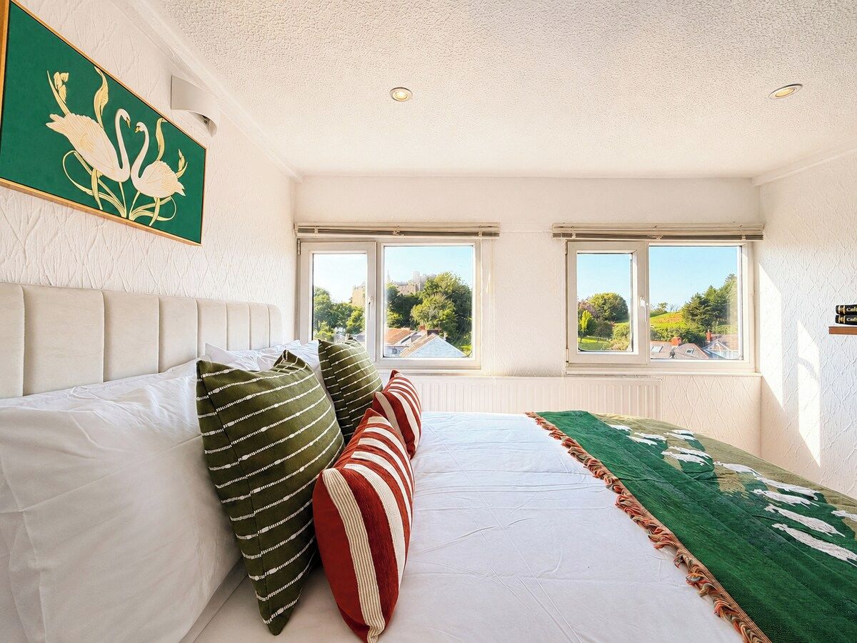 A bedroom with a bed, pillows, a green throw, and a window with a view.